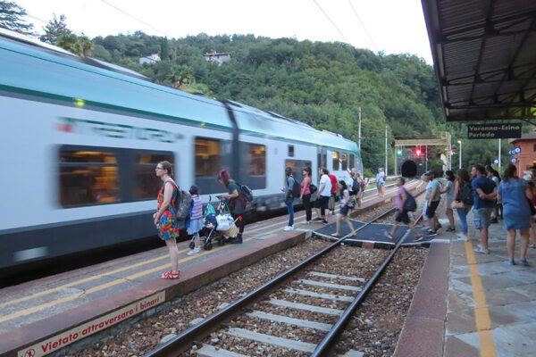 An Italian regional train is pulling into the Varenna station, people are preparing to board.