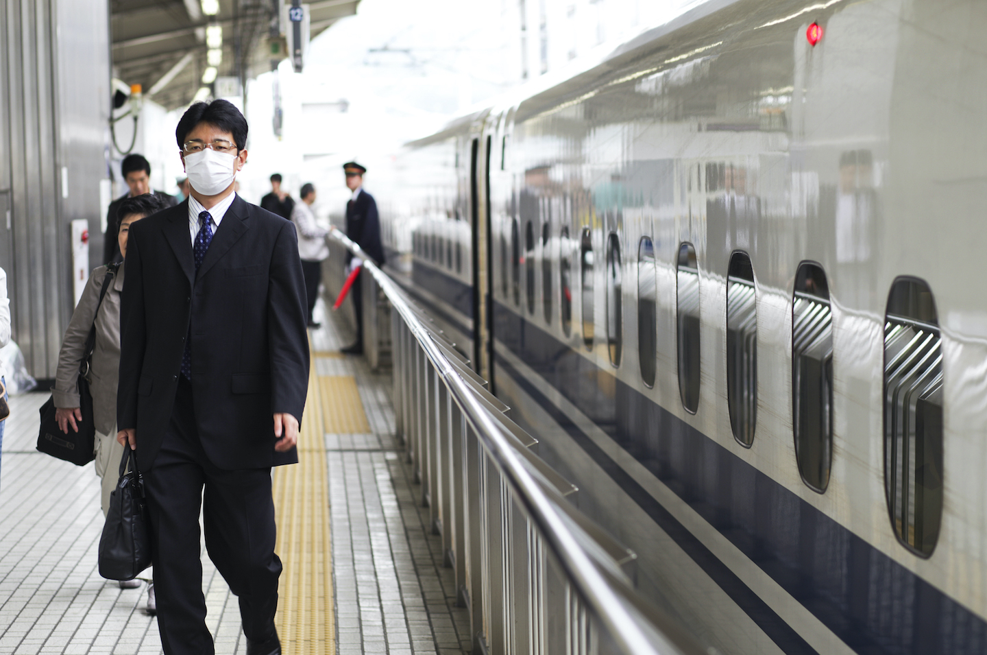 A man has just dis-embarked from a Japanese bullet train wearing a mask.