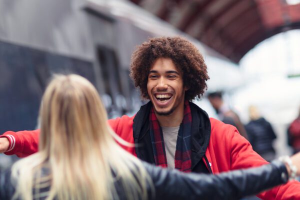 A man has gotten off a train. A woman is greating him with a hug.