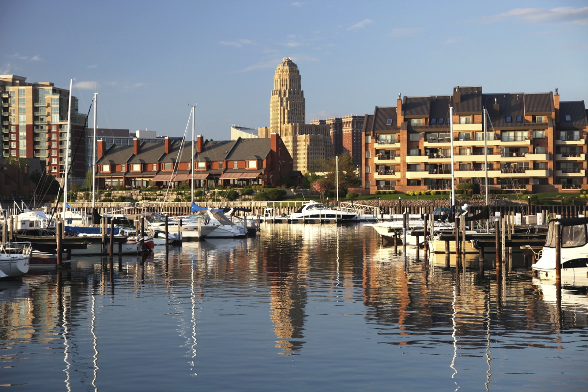 Sail boats are in the harbor with the Buffalo City Hall in the background.