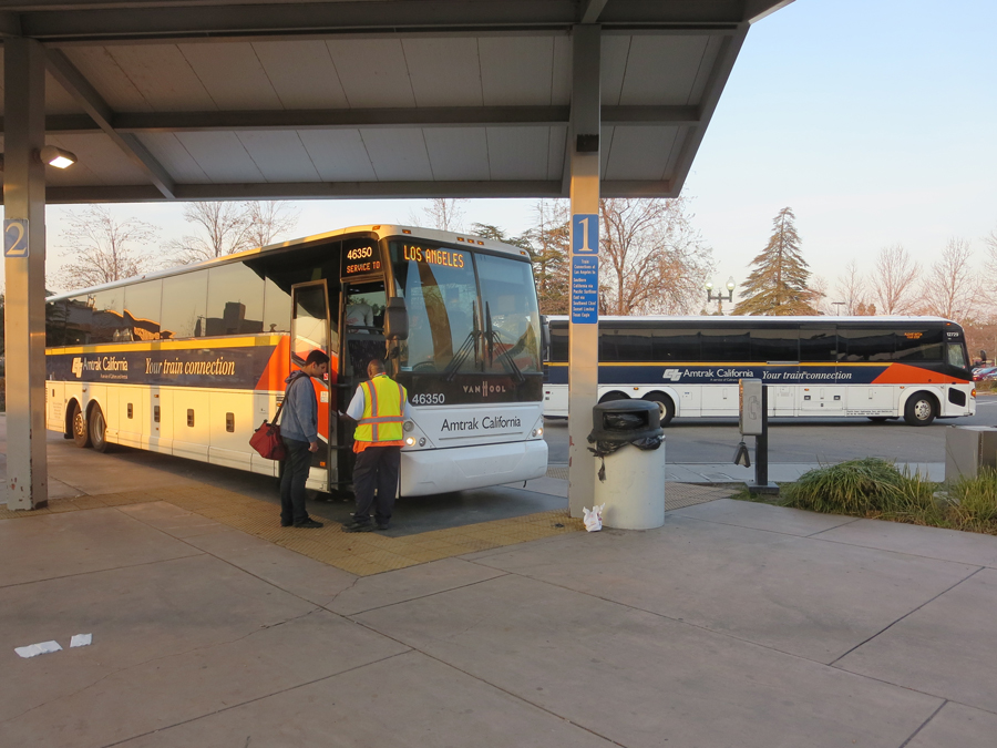 A passenger is about to board an Amtrak bus at Bakersfield CA.  Another Amtrak bus is leaving the station.