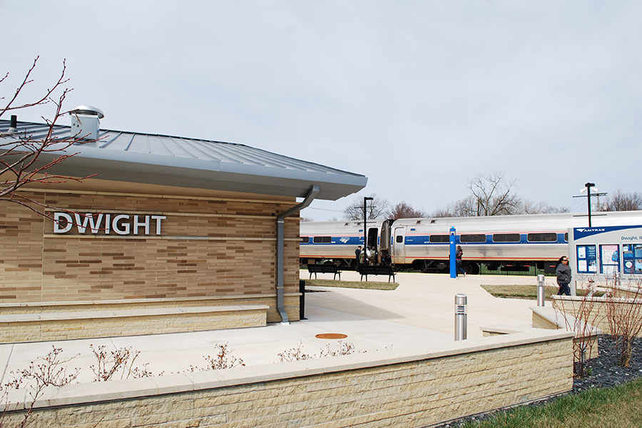 The new Dwight station is in the foreground. An Amtrak train is stopped at the platform in the background.