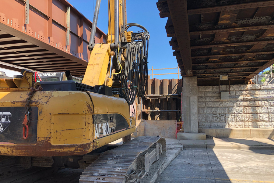 A crane is in the foreground between tow bridges.  The one on the right is new, the one on the left will be replaced.