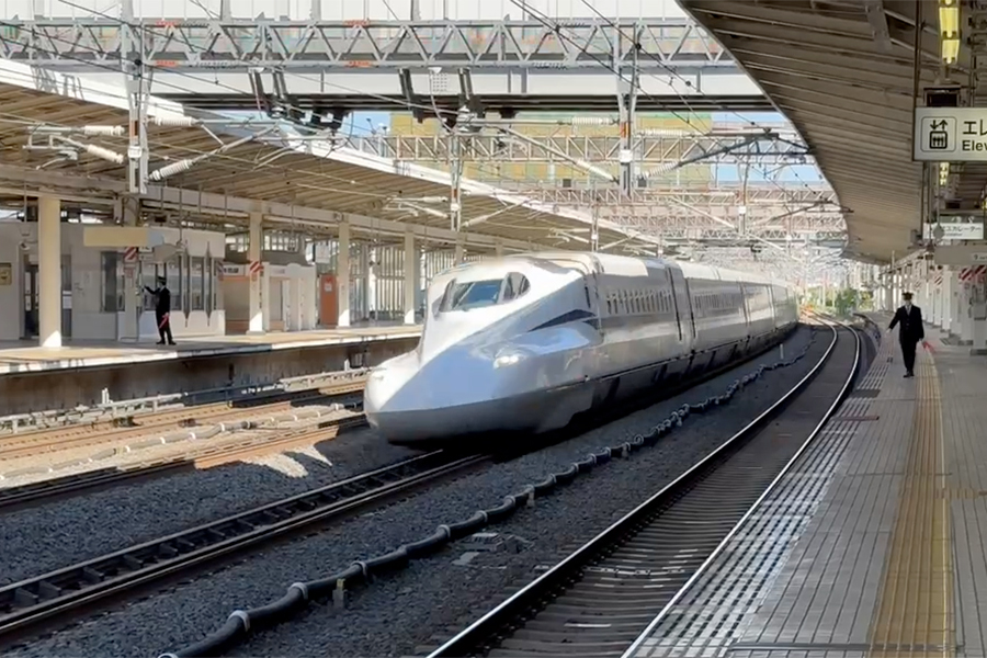 A Japanese high-speed train is passing a station on a curve.