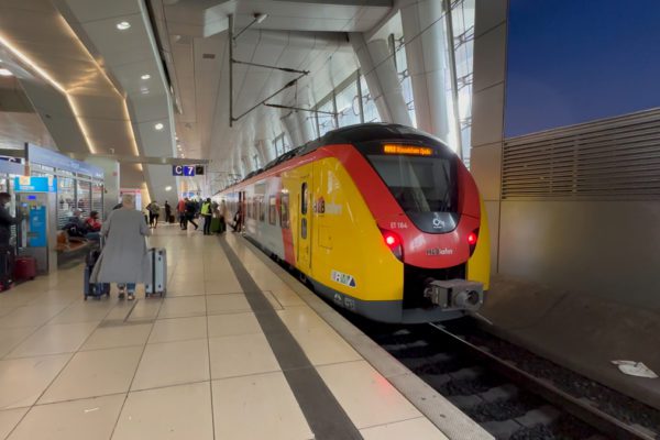 A regional train is stopping at Frankfurt airport station in Germany. Woman is rolling luggage to get on train.