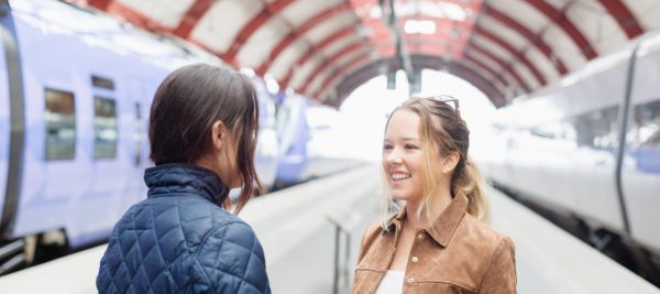 Two woman are happy to see each other on station platform with two trains.