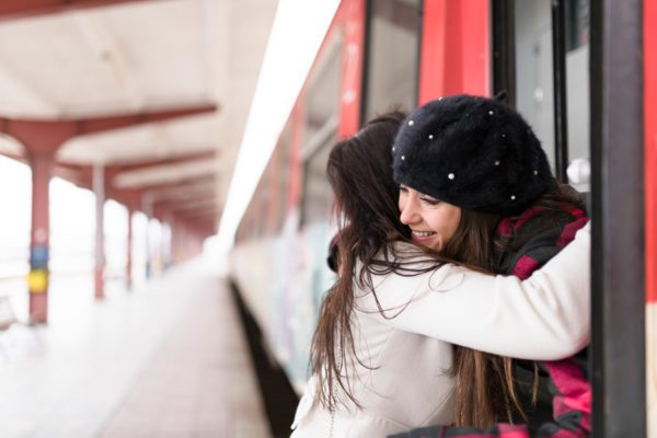 Two women are hugging. One is standing on the train platform, the other is on the train. It is snowing.