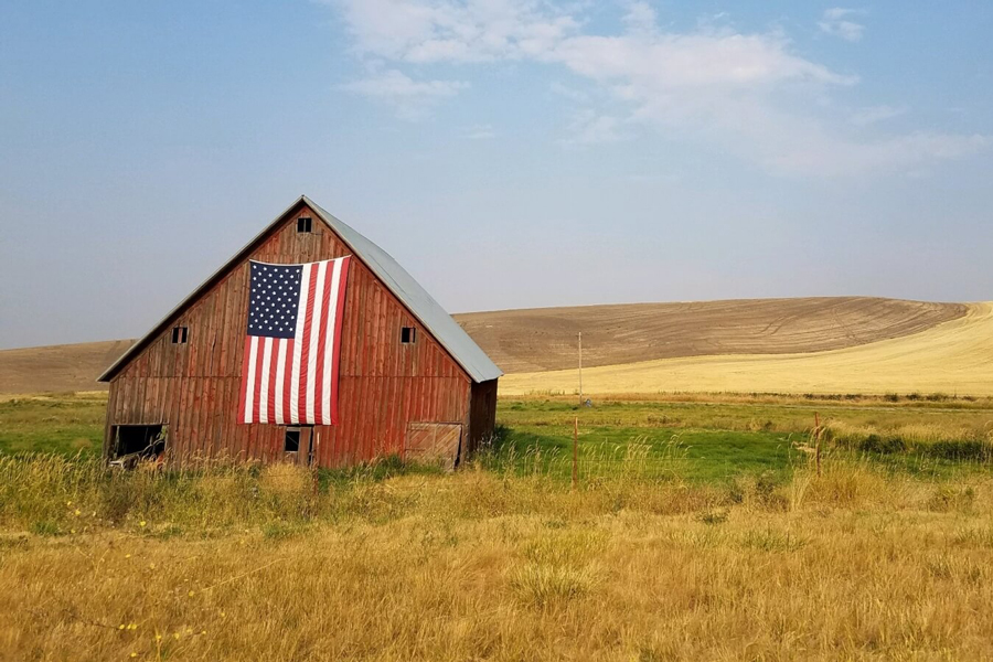 A red barn in a field with an American flag hanging on the side.