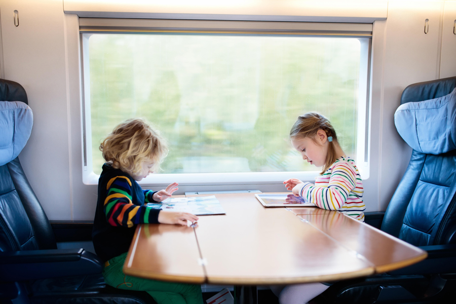 A boy and girl are working on tablets at a table on a high-speed train.