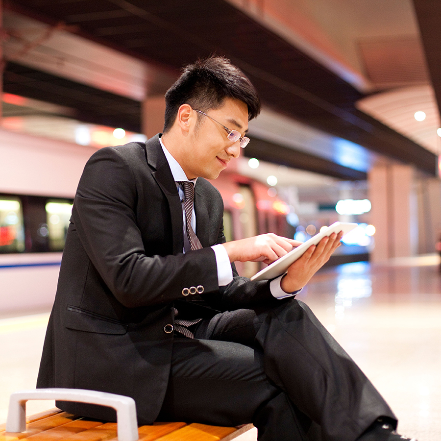 Dude using an IPad on a railroad platform in China with high-speed train in background.