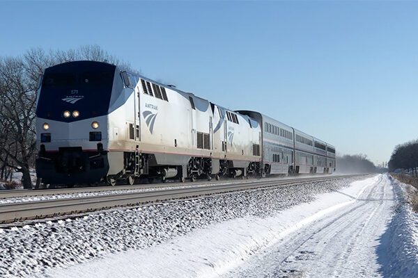 An Amtrak passing by in the snow. It has two locomotives and 4 cars.