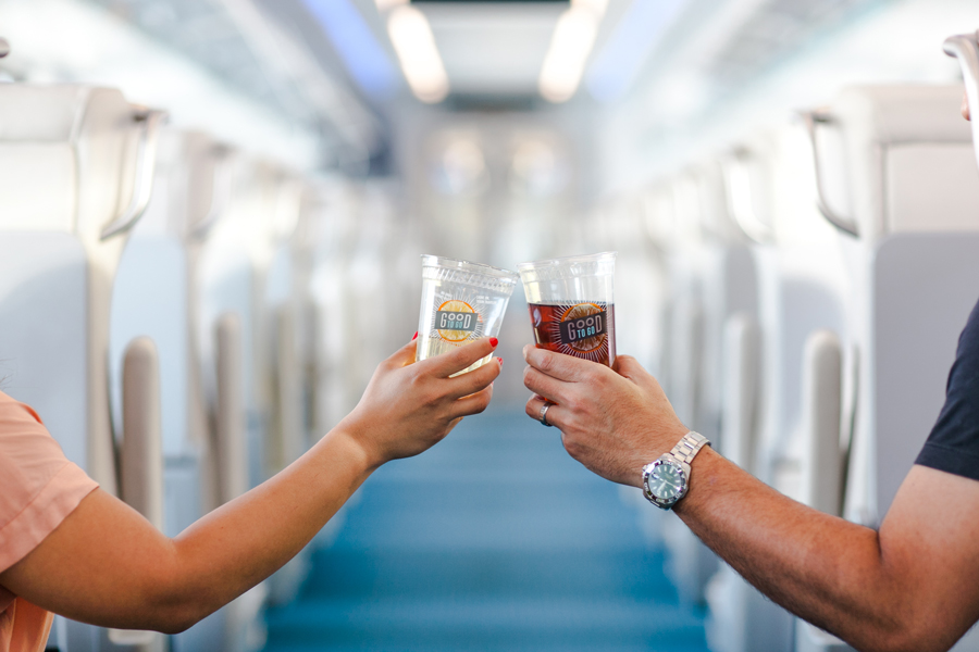 Two people are toasting across the aisle in a Brightline train.