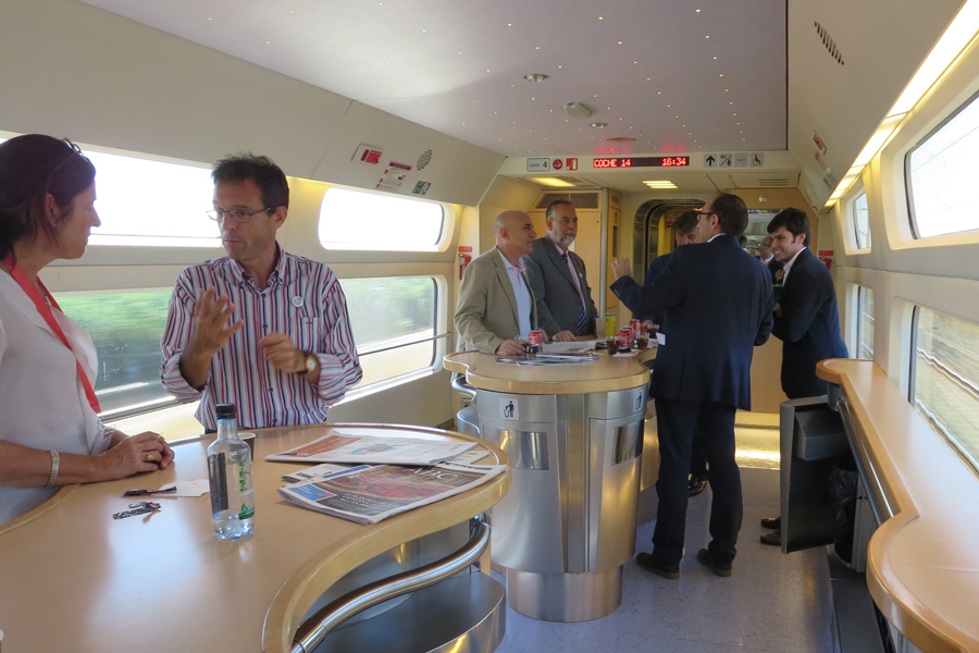 two groups of people are having a conversation on a Spanish high-speed train going 186-mph.