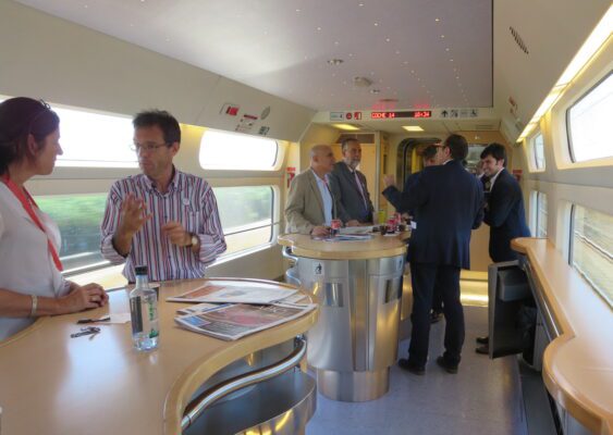 two groups of people are having a conversation on a Spanish high-speed train going 186-mph.