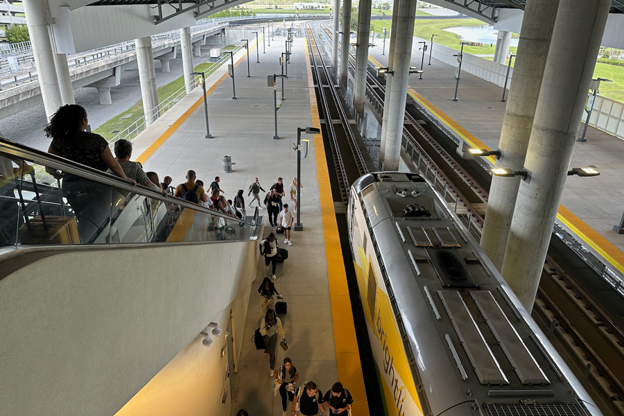 Passenger are descending on the escalator to platform level where a Brightline train is waiting.