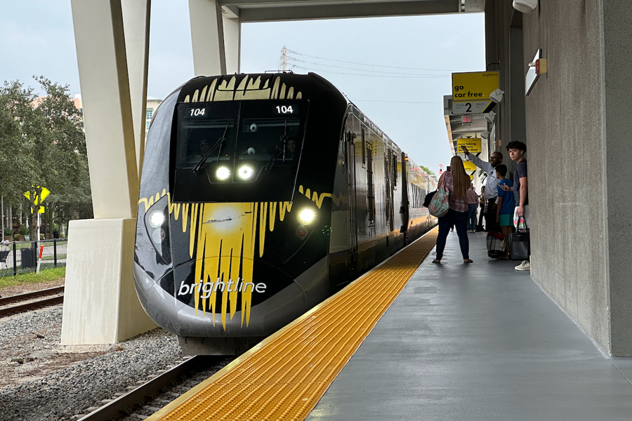 A Brightline train bound for Miami is pulling into West Palm Beach station.  A passenger is waving to the engineer.