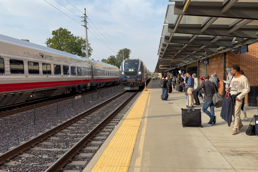 A crowd of passengers is waiting on the station platform at Normal, IL as the northbound train arrives. The southbound train is on the opposite track.
