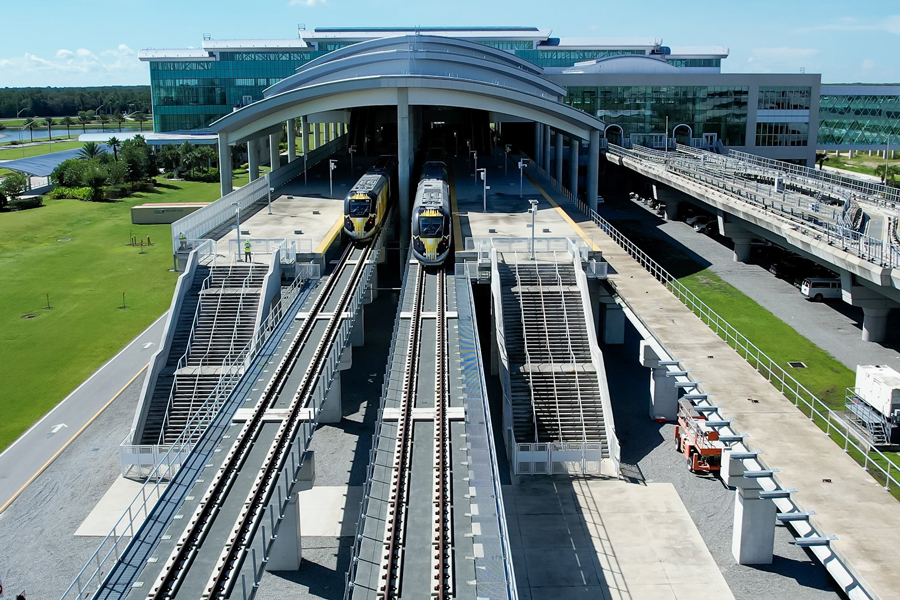 A drone shot looking down on the Brightline Orlando station from the north with two trains in the station.