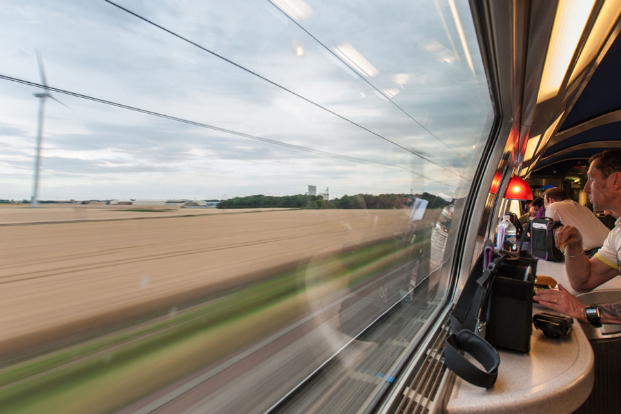 A man is looking out the window of a TGV high-speed train at blurred farm field with a windmill.