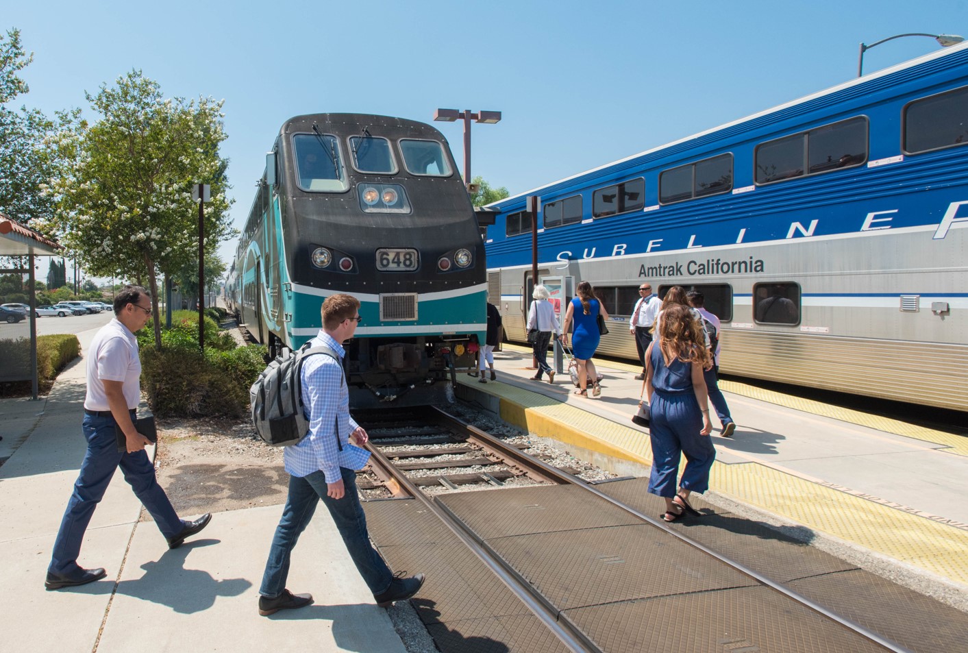 Passengers are passing by a Metrolink train to board an Amtrak train in southern California.