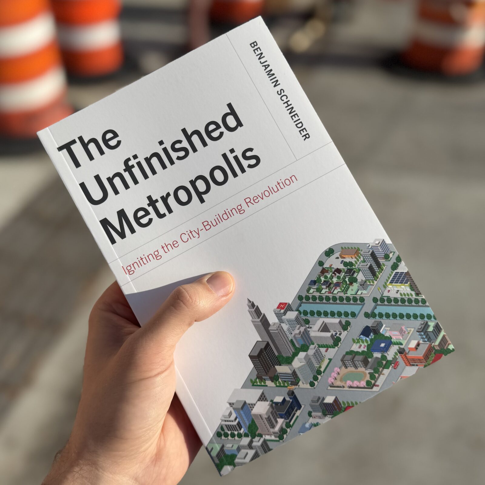 A copy of "The Unfinished Metropolis" with construction cones in the background