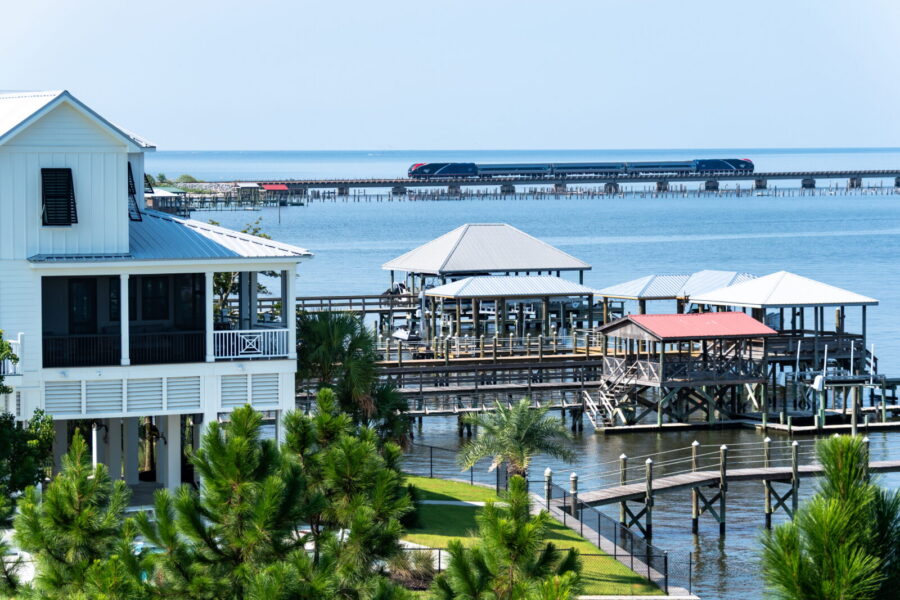 Coastal houses and docks in the foreground with the ocean in the background. A train crosses a viaduct over the water in the distance.