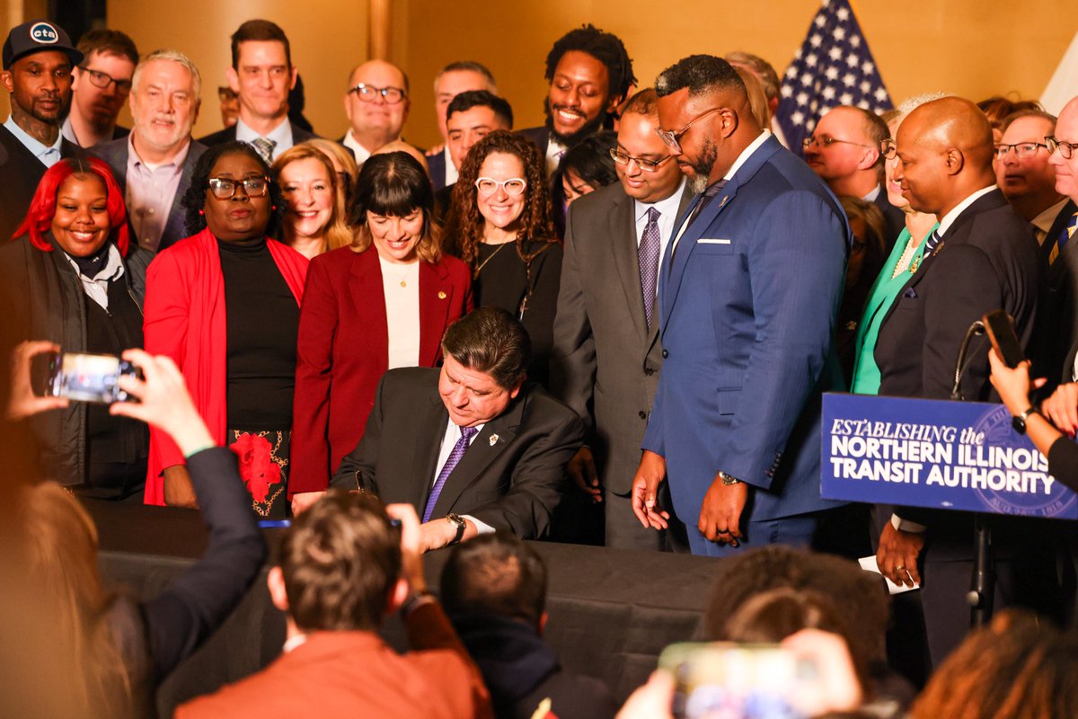 Illinois Governor Pritzker is signing a major transit program bill with a crowd behind him.