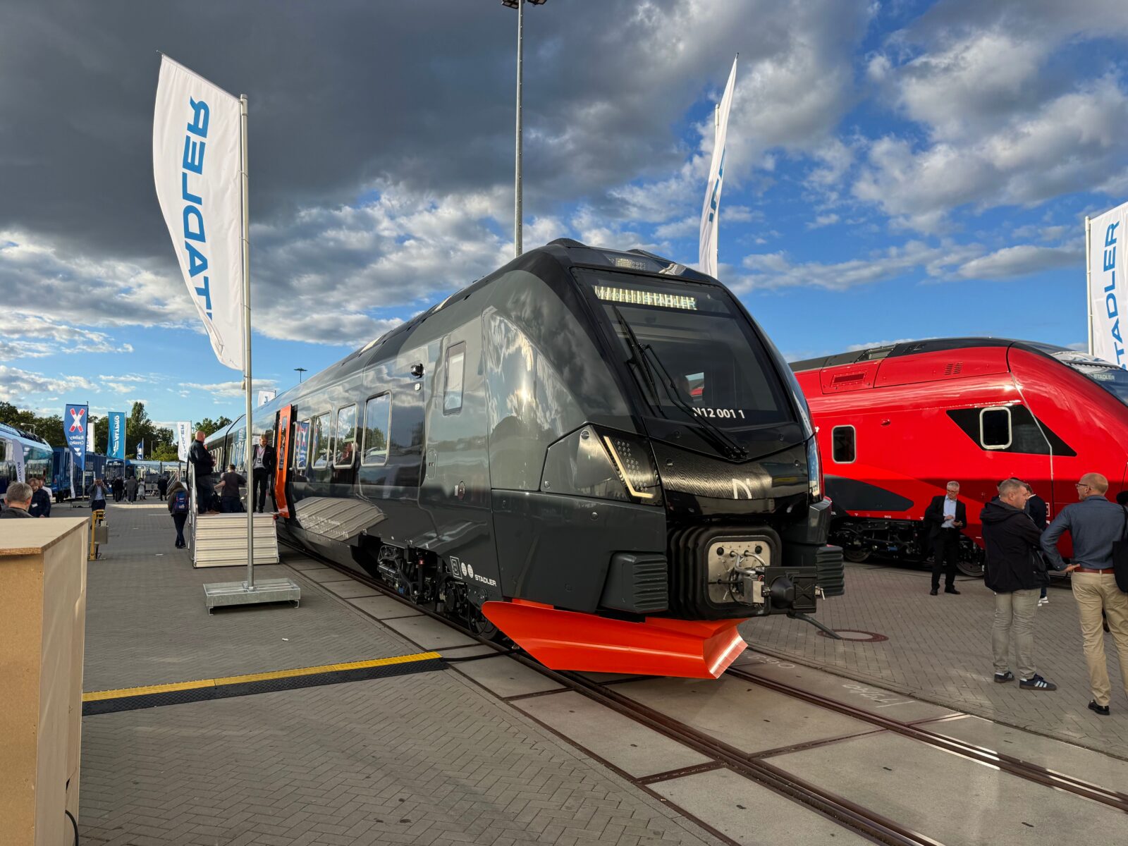 A sleek, black, gray, and orange electric trainset at the outdoor InnoTrans railyard in Berlin, Germany